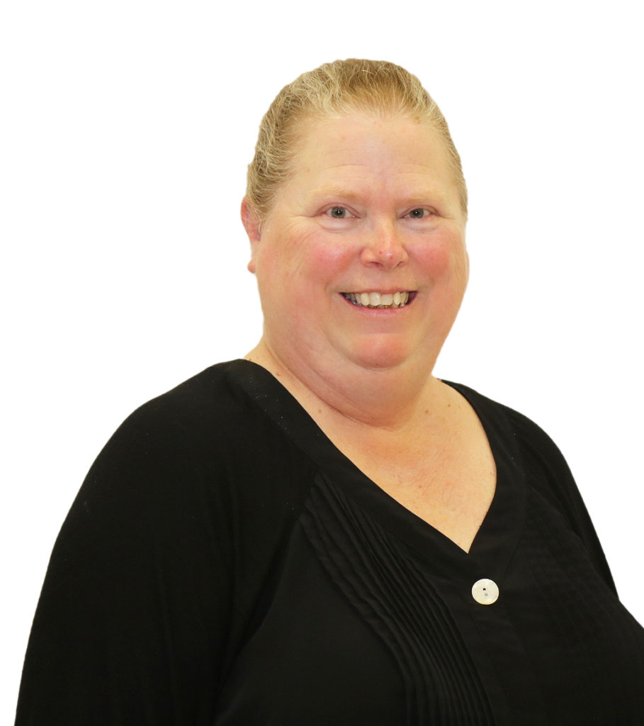 The image shows a woman smiling warmly against a plain white background. She has her blonde hair pulled back neatly and is dressed in a black blouse with pleated detailing on the front, fastened with a single white button. Her expression is cheerful and friendly, giving off a positive and approachable vibe. The image appears to be a professional portrait, presenting a welcoming and professional demeanor.