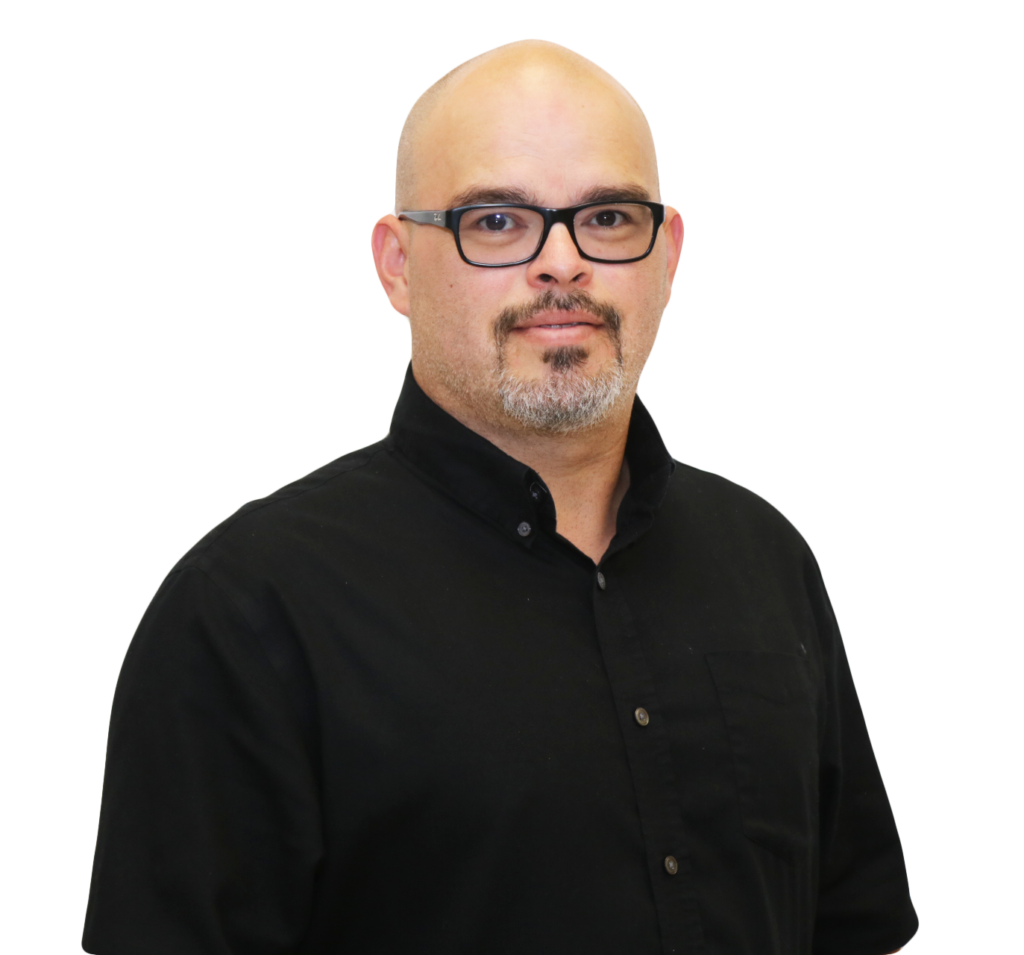 The image shows a man standing against a plain white background. He has a bald head and wears black-rimmed glasses. He has a light goatee and mustache, giving him a neatly groomed appearance. He is dressed in a black button-up shirt with the top button open, and his expression is calm and composed, conveying a professional demeanor. The image appears to be a professional business portrait.